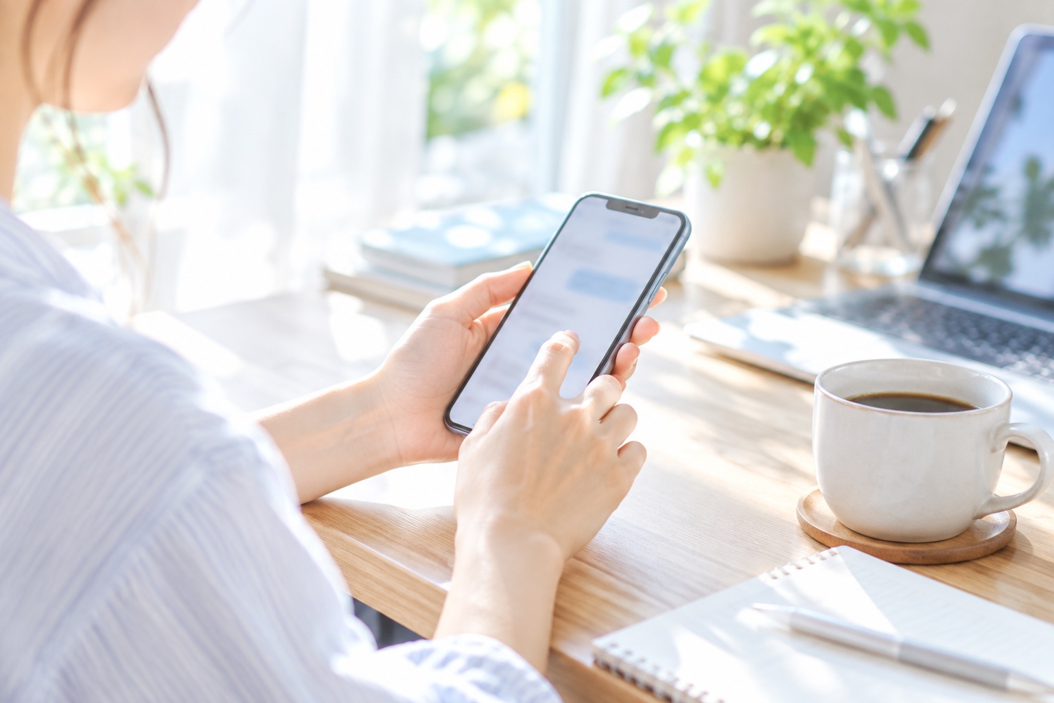 朝の自宅のデスクで、スマートフォンから以前の取引先に近況のメッセージを送るフリーランス