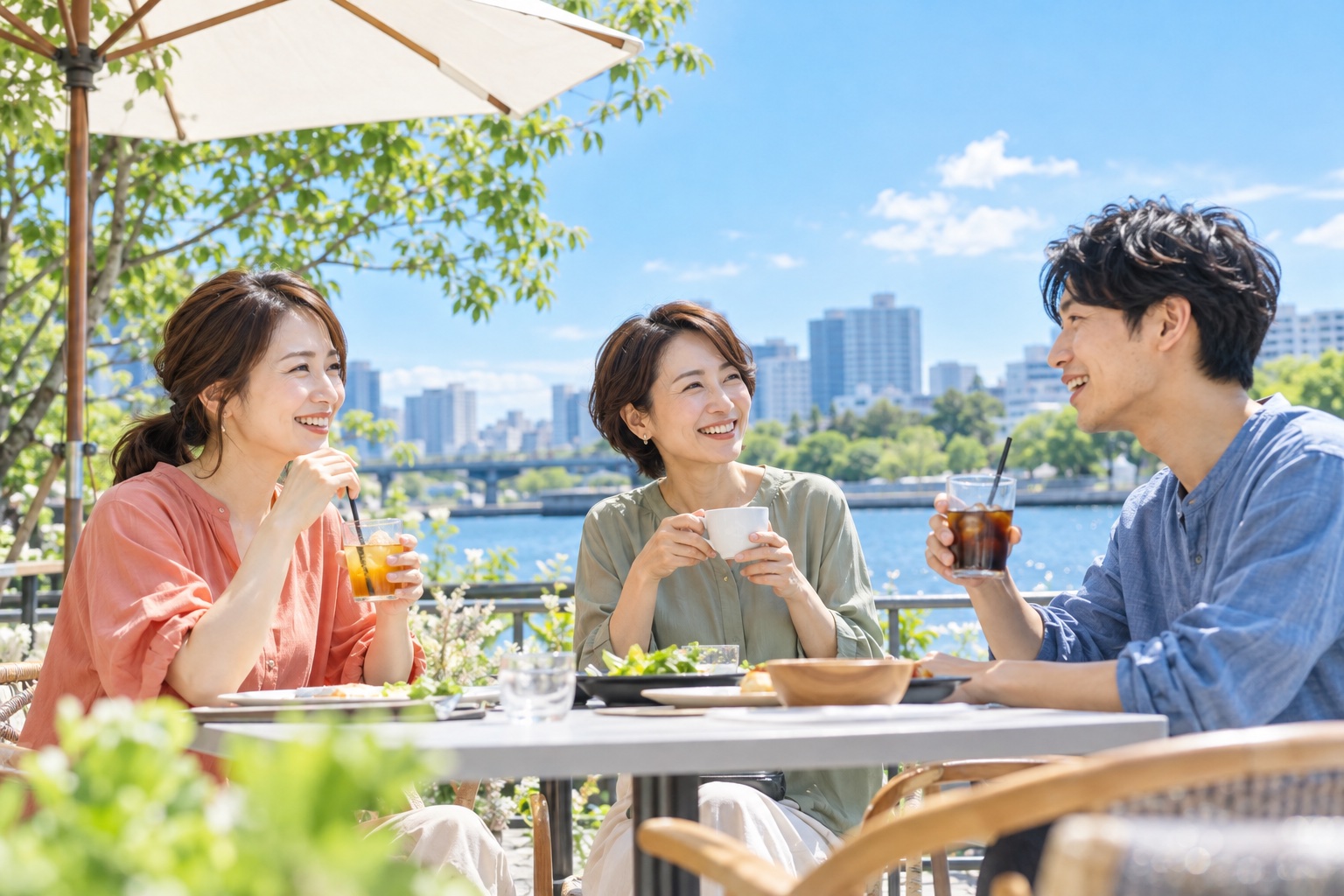 晴れた昼の川沿いのカフェのテラス席で、飲み物を手に働き方を相談し合う3人のフリーランス仲間